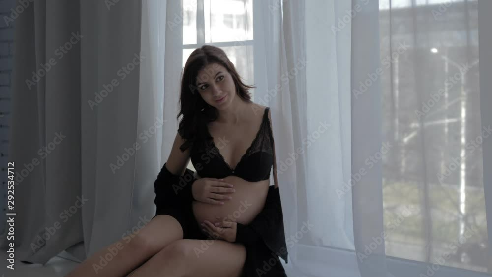 Pregnant Woman Sitting On The Windowsill At The Window And Posing Pregnant Woman Sitting On The Windowsill At The Window And Posing