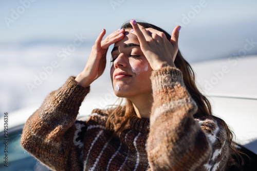 Young woman applying sunscreen on her face in snow landscape