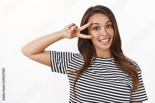 Close-up cute friendly-looking stylish young brunette in striped t-shirt showing peace, victory sign near eye smiling delighted, express joy and wellbeing, lead happy lifestyle, white background