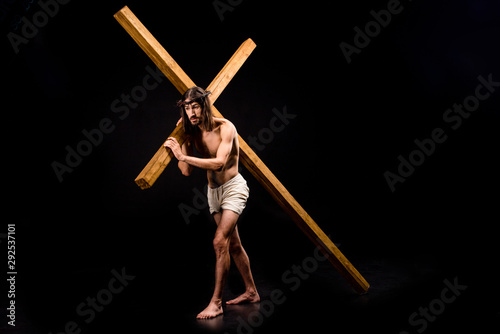 shirtless jesus in wreath holding wooden cross and walking on black photo