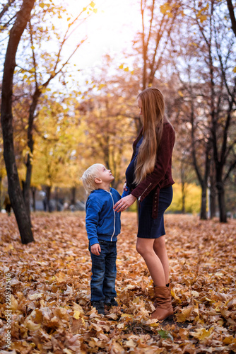 Little blond boy and his pregnant mom's belly. Autumn park on the background