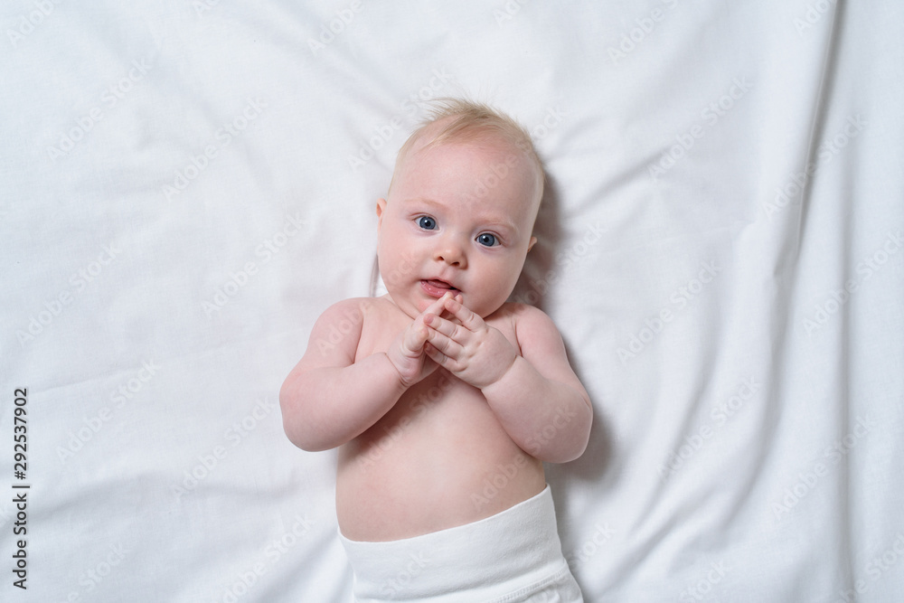 Portrait of a cute blond baby on a white sheet. Top view Portrait of a cute blond baby on a white sheet. Top view