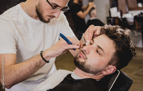 Young man with trendy haircut at barber shop. Barber does the hairstyle and beard trim.