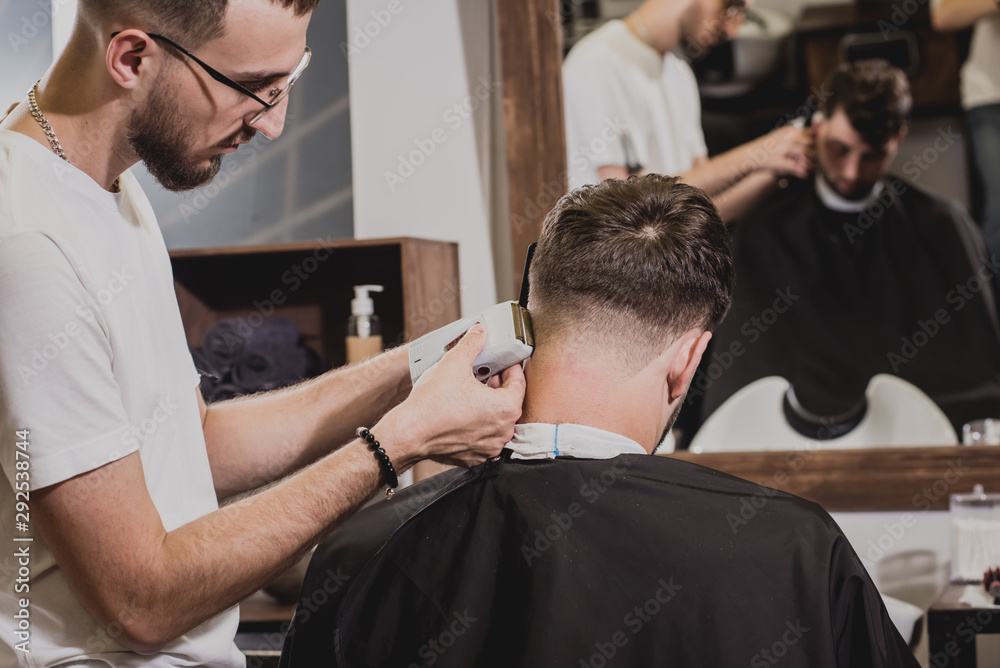 Young man with trendy haircut at barber shop. Barber does the hairstyle and beard trim. Young man with trendy haircut at barber shop. Barber does the hairstyle and beard trim.