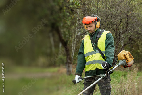 A working man in professional outfit mows grass with a trimmer, a mower. Mowing lawns, roadsides, edge