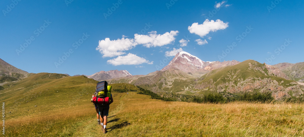 Very beautiful view of the Mount Kazbek, the second highest peak in Georgia with background of cloud. Hiker trekking on the mountains, he is carrying a backpack and hiking equipment