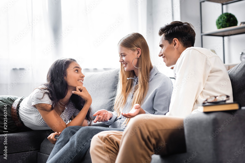 handsome and attractive multicultural friends smiling and talking in apartment