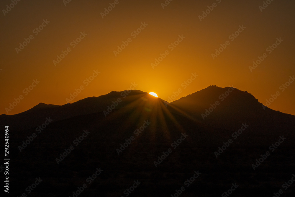 Sun peaking over mountains at sunrise in the mojave desert