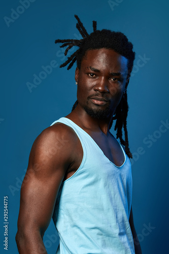 sexy young muscular man in white shirt looking at the camera, isolated blue background, studio shot. © the faces