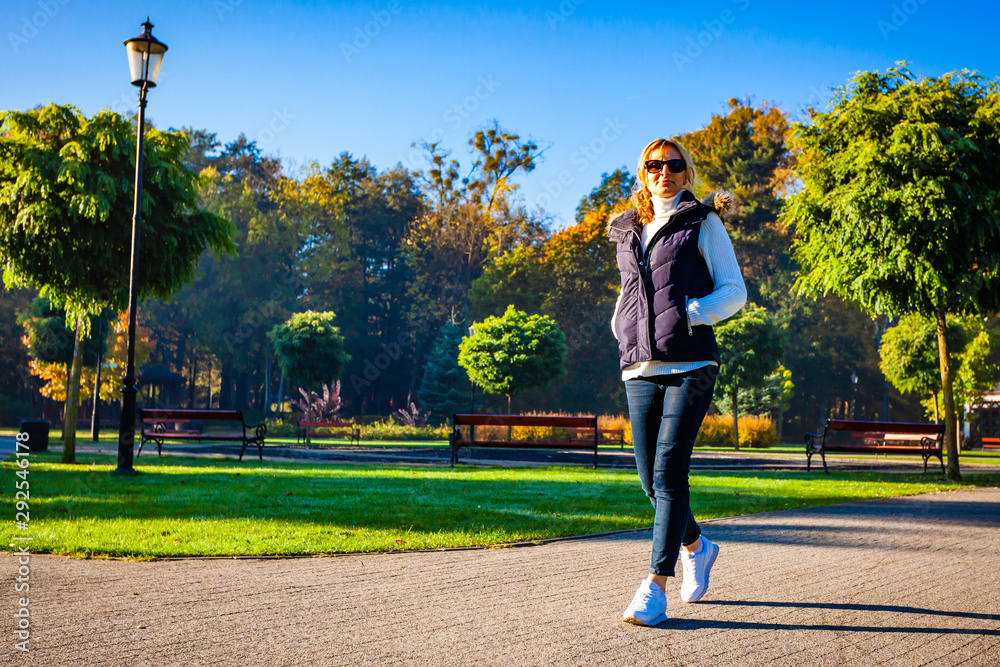 Middle-aged woman walking in city park - obrazy, fototapety, plakaty 