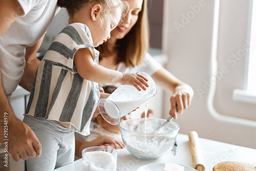 cute girl adding milk to a bowl with dough, close up cropped side view photo
