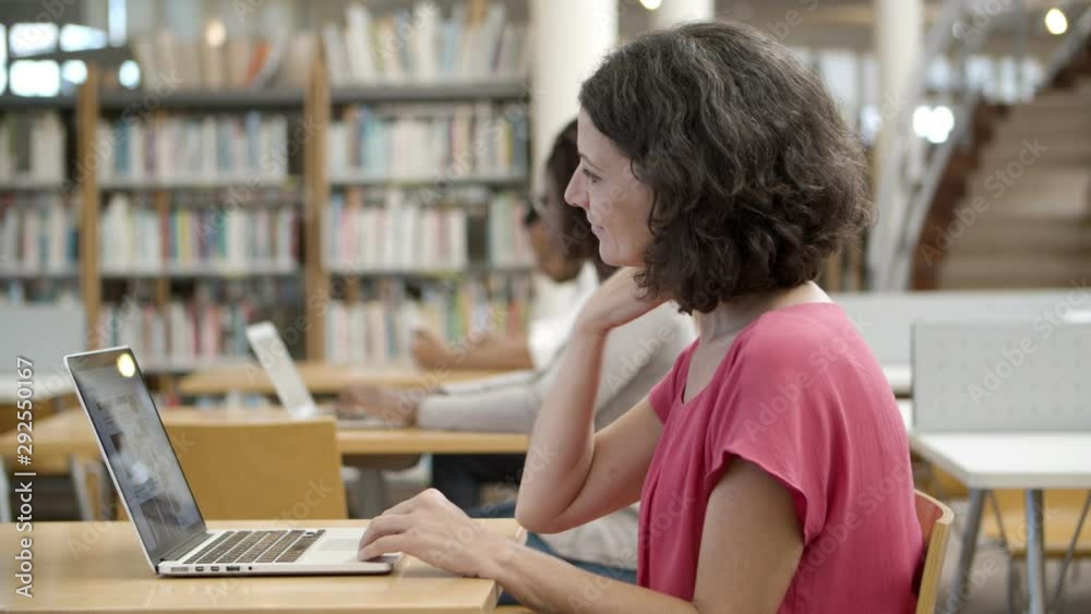 Beautiful curly brunette sitting at table with laptop. Side view of thoughtful mature woman using laptop. Education concept Beautiful curly brunette sitting at table with laptop. Side view of thoughtful mature woman using laptop. Education concept