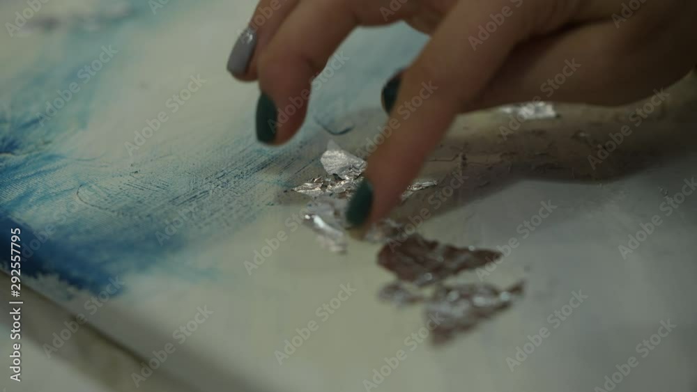 Woman apply silver leaf imitation on blue and white painting. Close up of hand