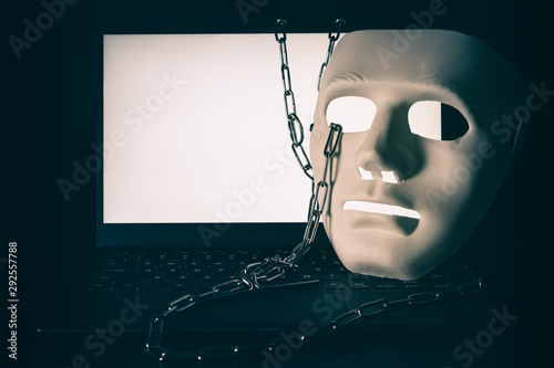 Laptop with chains and white mask on black isolated. Data, Cyber internet safety, Firewall and Security concept