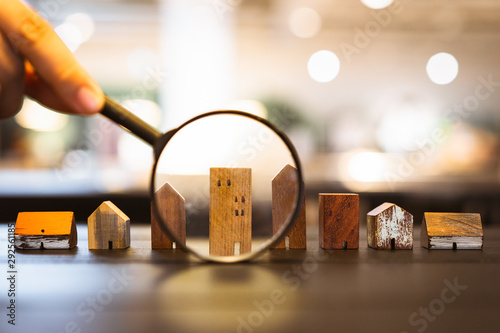 Hand holding magnifying glass and looking at house model, house selection, real estate concept. photo