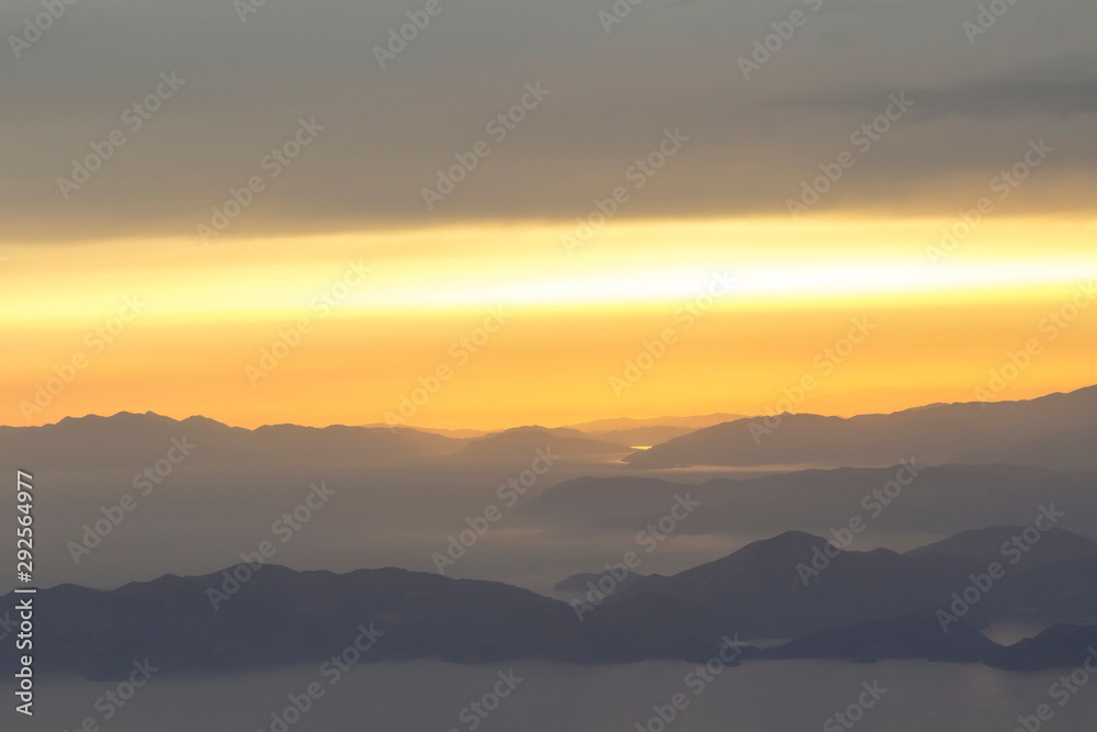 Mediterranean landscape. Sunset on the sea with flowing bright colored rays of the sun through the clouds. Silhouettes of mountains.  Background, blur.