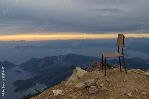 Sunset on the sea with pouring bright sun rays through the clouds. A chair on top of a mountain..