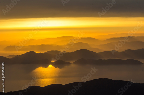 Mediterranean landscape. Sunset on the sea with flowing bright colored rays of the sun through the clouds. Silhouettes of mountains.  Background  blur.