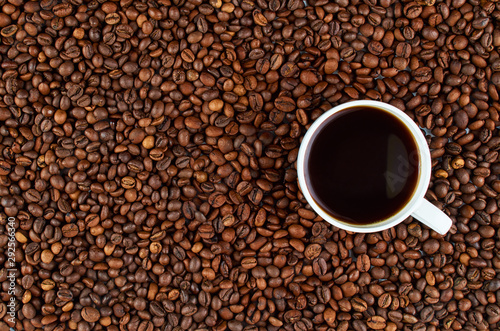 Background of roasted coffee beans. In the foreground is a white coffee Cup with coffee.