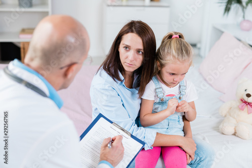 Worried mother listening to doctor advice while holding her sick little daughter