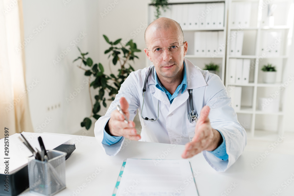 Confident young doctor in whitecoat and eyeglasses explaining something to you