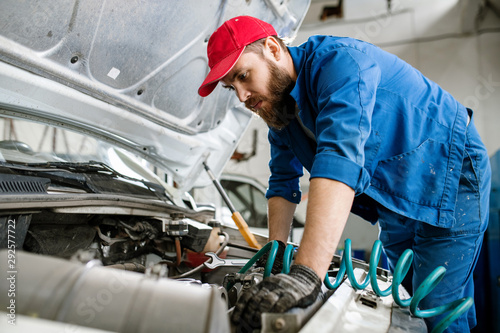 Bearded technician of car repair service examining engine of broken vehicle