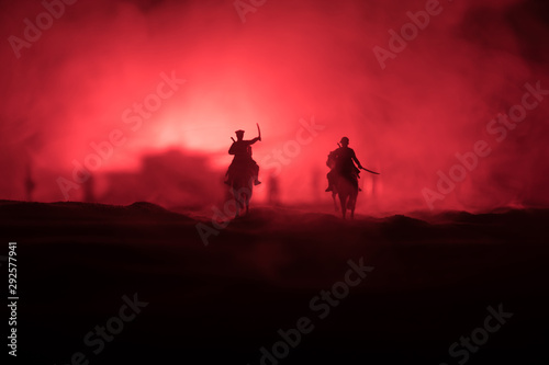 World war officer  or warrior  rider on horse with a sword ready to fight and soldiers on a dark foggy toned background. Battle scene battlefield of fighting soldiers.
