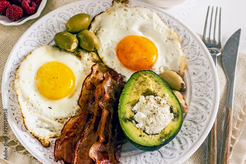 Keto Diet LCHF Keto breakfast. Fried eggs with bacon, avocado, cream cheese, nuts, olives and coffee on a white plate on a light background. Low carb diet concept. high fat diet. Keto bacon and eggs 