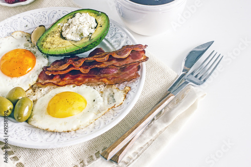 Keto Diet LCHF Keto breakfast. Fried eggs with bacon, avocado, cream cheese, nuts, olives and coffee on a white plate on a light background. Low carb diet concept. high fat diet. Keto bacon and eggs 