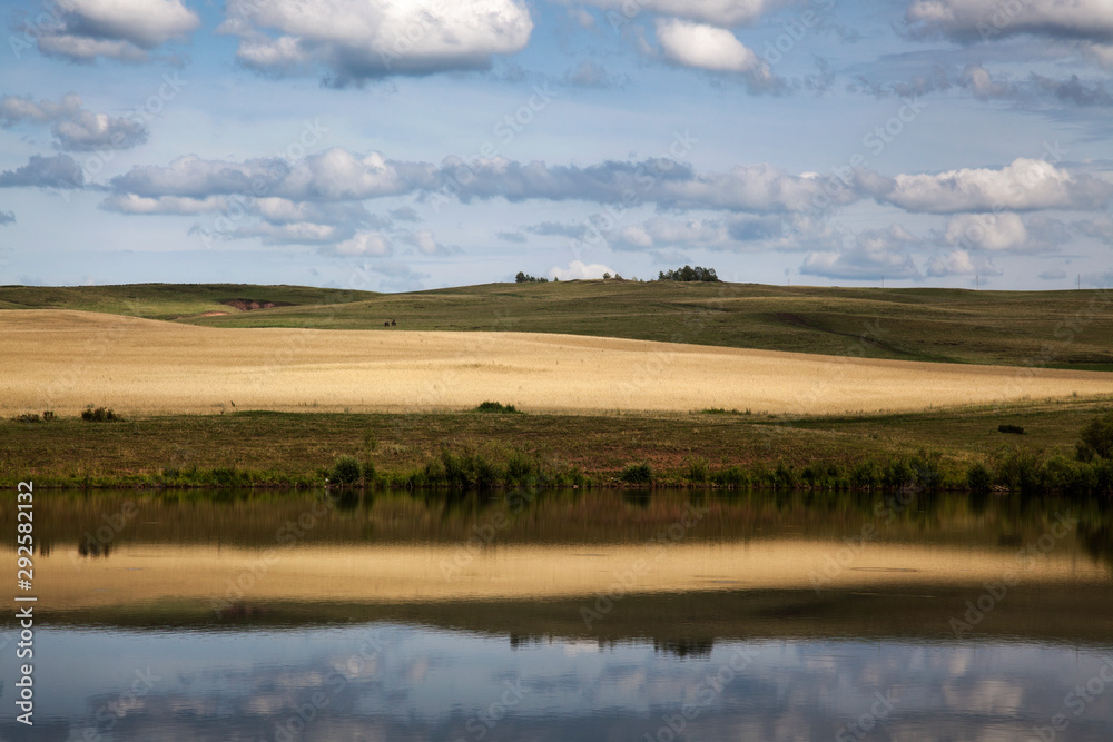 Reflection of yellow fields and cloudy sky in the lake.