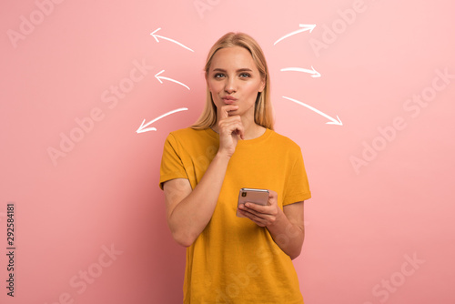Blonde girl thinks about the right option. Confused and pensive expression. Pink background photo