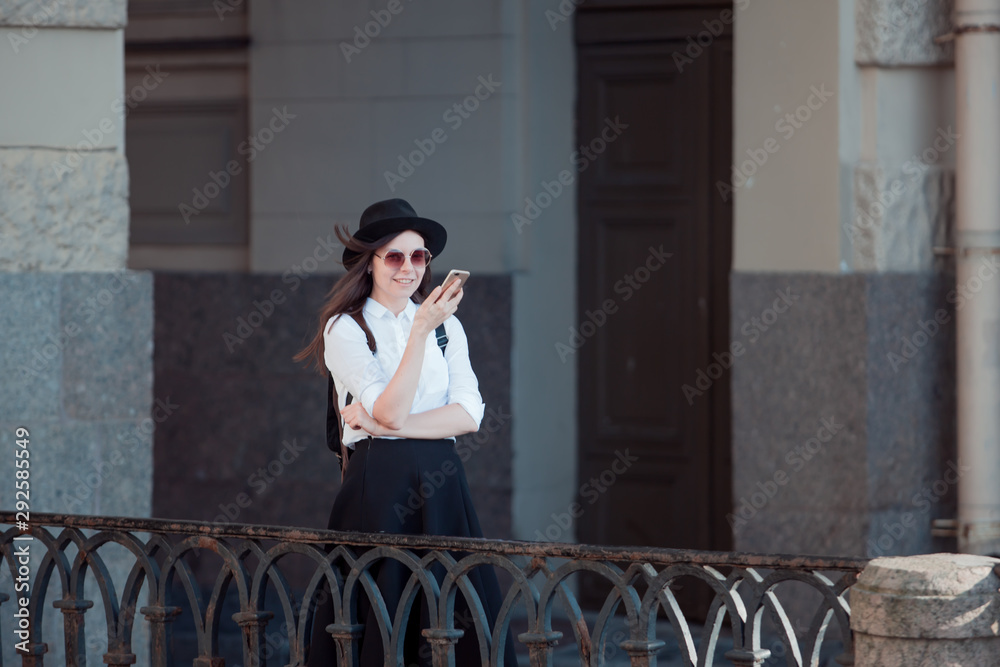 young woman in a hat and with a backpack walks in the city and uses a smartphone. young woman in a hat and with a backpack walks in the city and uses a smartphone.
