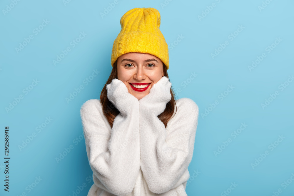 Portrait of happy female with red lips, white perfect teeth, beaming smile, wears comfortable long sleeved sweater, looks directly at camera, holds chin has pleasant feelings after unforgettable date Portrait of happy female with red lips, white perfect teeth, beaming smile, wears comfortable long sleeved sweater, looks directly at camera, holds chin has pleasant feelings after unforgettable date