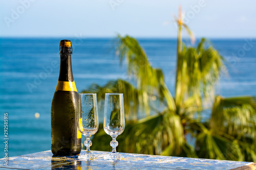 Romantic event  bottle with cold sparkling wine  cava or champagne served with two glasses on table with sea view and palm tree