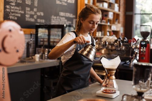 Professional barista preparing coffee using chemex pour over coffee maker and drip kettle. Young woman making coffee. Alternative ways of brewing coffee. Coffee shop concept. photo