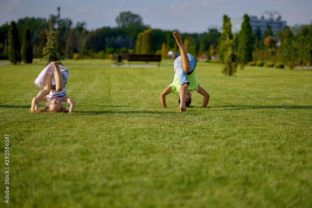 two happy smiling children tumbling on green grass. Cheerful brother and sister laugh together. Happy kids have fun on the park lawn. Children's day