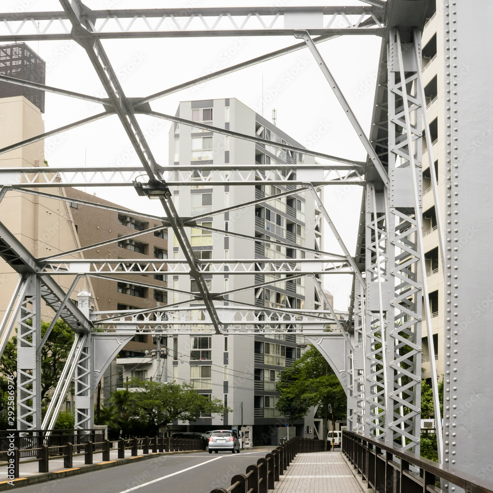 Abstract urban or transportation background featuring details of gray steel bridge frames with rivets and buildings behind in downtown Tokyo Japan. 