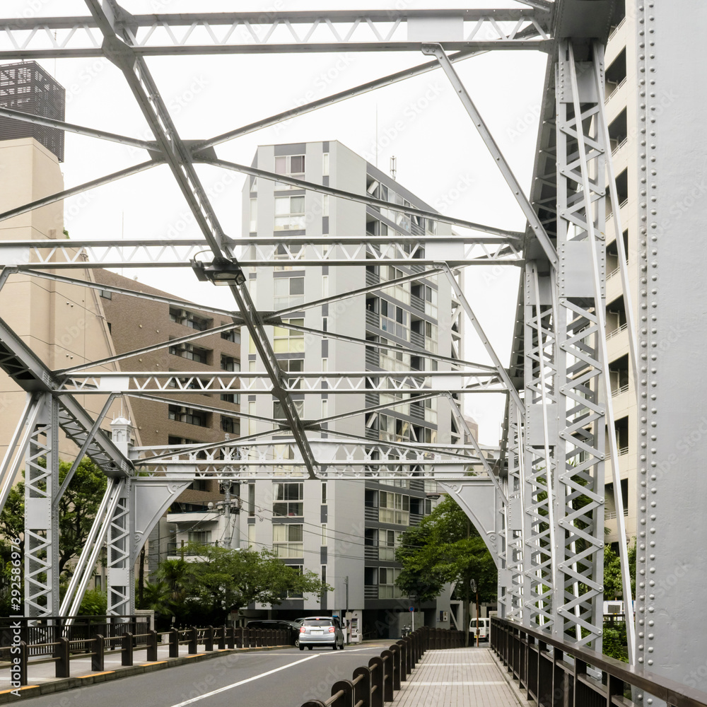 Abstract urban or transportation background featuring details of gray steel bridge frames with rivets and buildings behind in downtown Tokyo Japan. Abstract urban or transportation background featuring details of gray steel bridge frames with rivets and buildings behind in downtown Tokyo Japan.