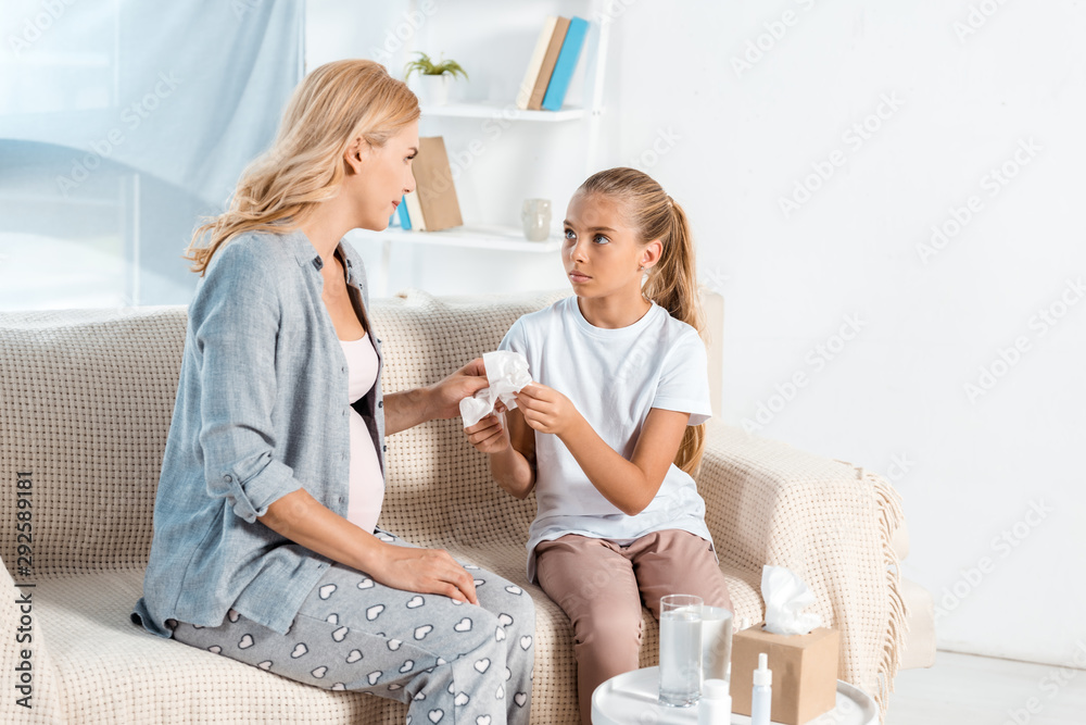 pregnant mother taking napkin near cute daughter near table with tissue box
