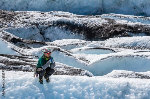 Glacier Guide crouched in his crampons on a slope observing other guides.