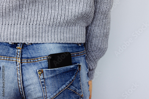 A mobile phone in the back pocket of a jeans on a girl in casual clothes.