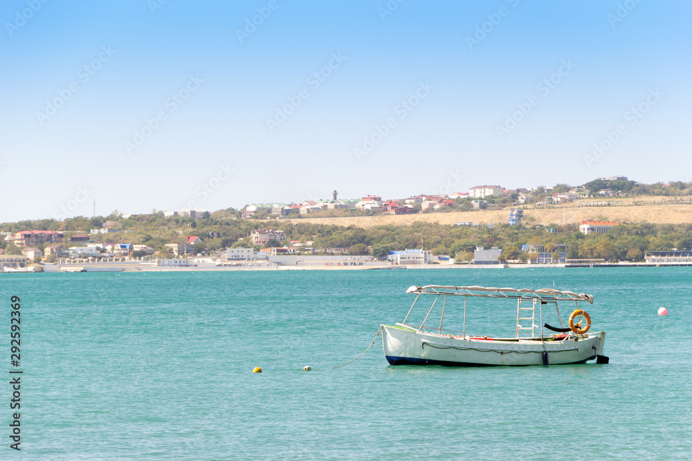 White boat anchored in a turquoise water of sea bay. Sea coast with residential buildings, pier and clear sky in frame. Vacation at sea.