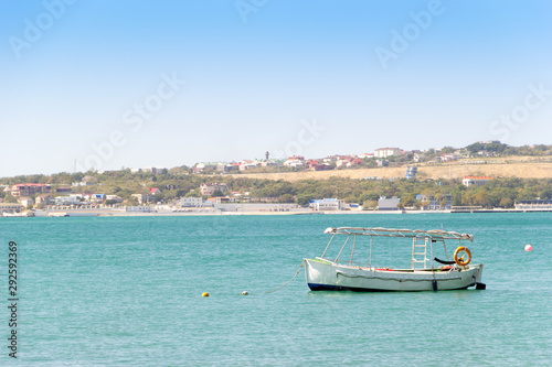 White boat anchored in a turquoise water of sea bay. Sea coast with residential buildings, pier and clear sky in frame. Vacation at sea. © Jekh