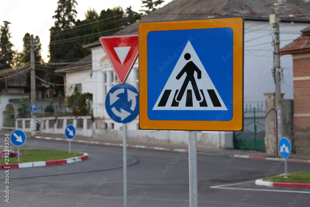 multiple street signs in a roundabout, pedestrian crossing, right of