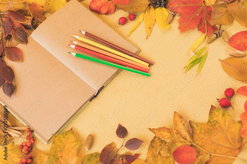 Open notebook  for records or drawing, a set of colored crayons in the framing of autumn leaves which  turn into the warm colors of orange, red, yellow and gold.