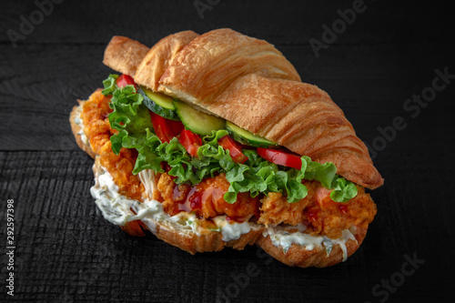Croissant sandwich with crispy chicken in batter, tomatoes, cucumbers, lettuce, sauce. Healthy, tasty, nourishing snack. Take away food