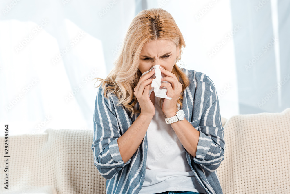 sick woman sitting on sofa and sneezing in napkin sick woman sitting on sofa and sneezing in napkin