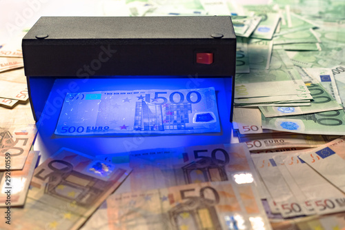 Money fake testing - euro banknotes authentication check in UV Currency Detector lights. Counterfeiting banknotes, checking at the bank by cashier, bank operator. Financial, banking concept.