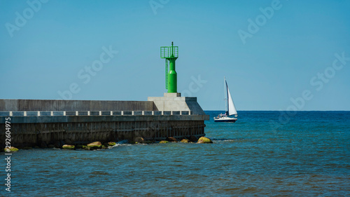 Modern lighthouse pole in green and boat entering sea gates in baltic sea, Pavilosta.