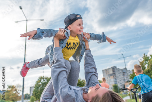 little boy in air plays, laughs, rejoices, young woman is mother with boy of 3-5 years old son, they play, they rest, on summer autumn day in city park, casual clothes are fun, joy is laughter.